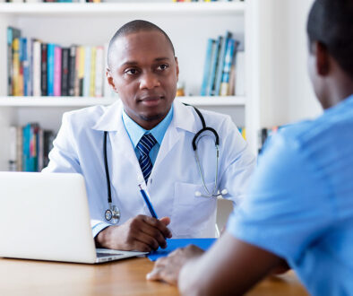 An African American Doctor Sitting at a Desk Listening Intently to a Patient Who Should See an Internist