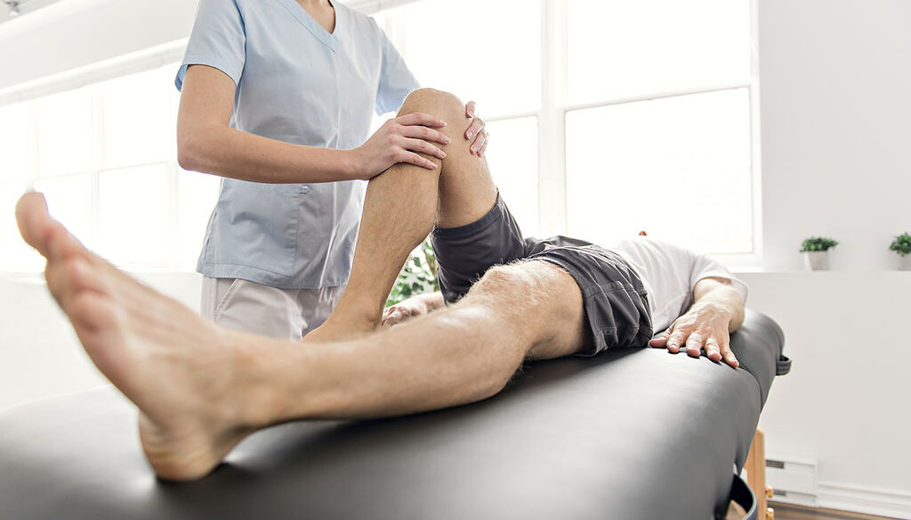 A Sports Medicine Doctor Holding an Athlete’s Knee Lying Down on a Massage Table