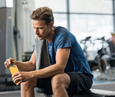 A Young Man Sitting on a Gym Bench Holding a Yellow Sports Drink in His Hands Testosterone Replacement Therapy Near Me