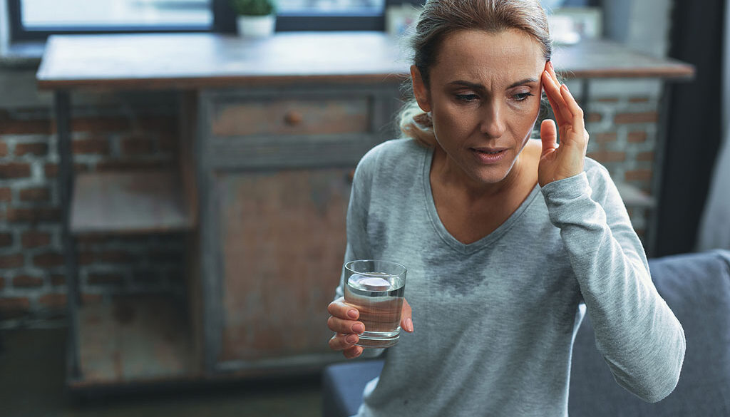 A Woman Sweating While Holding a Glass of Water and Rubbing Her Forehead Is Hormone Replacement Therapy Safe