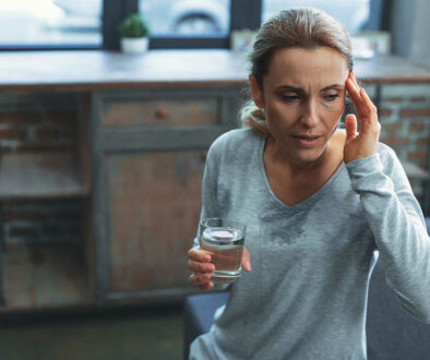 A Woman Sweating While Holding a Glass of Water and Rubbing Her Forehead Is Hormone Replacement Therapy Safe