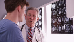 A Doctor Discussing Delayed Concussion Symptoms With a Young Male With Brain Scans in the Background