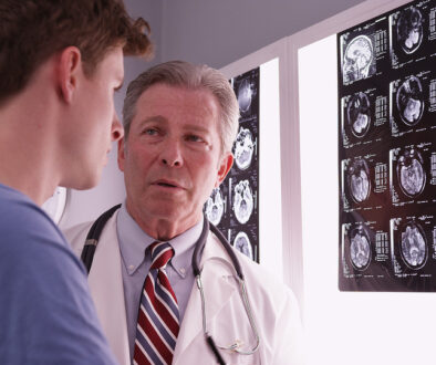 A Doctor Discussing Delayed Concussion Symptoms With a Young Male With Brain Scans in the Background